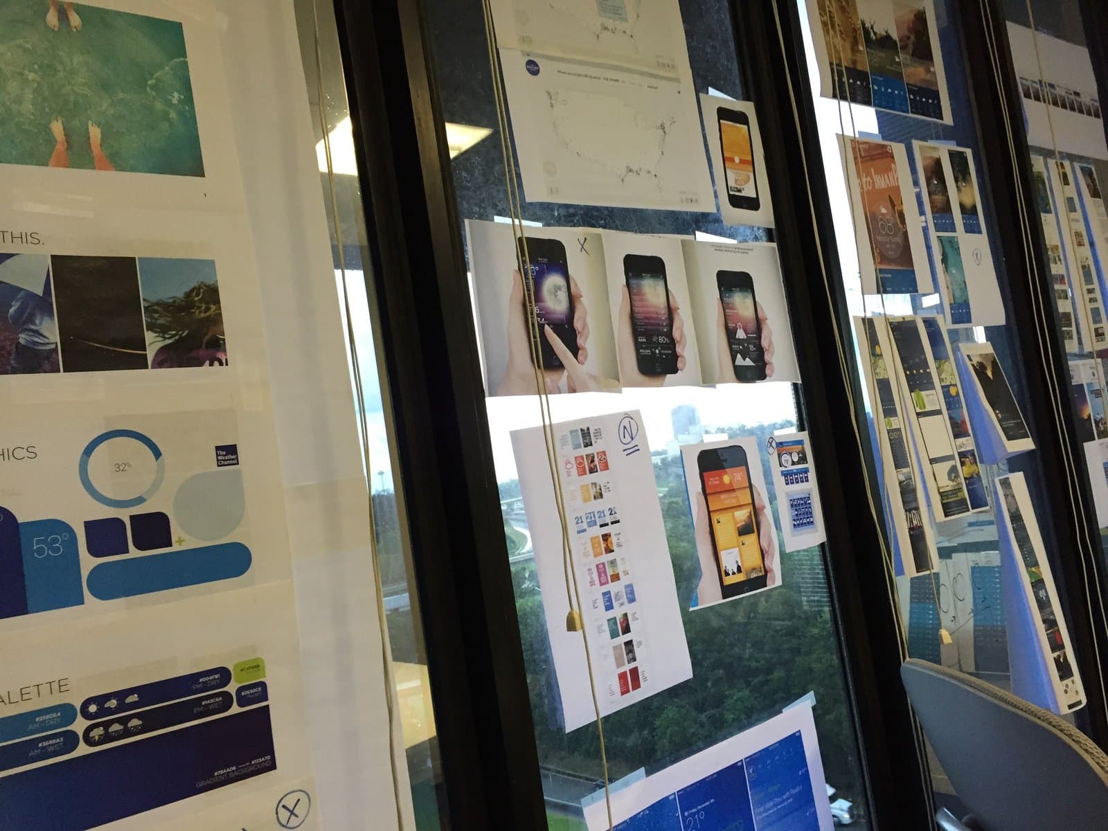 Weather Channel team critique, full glass wall covered in printed app designs, color palettes, and phone mockups